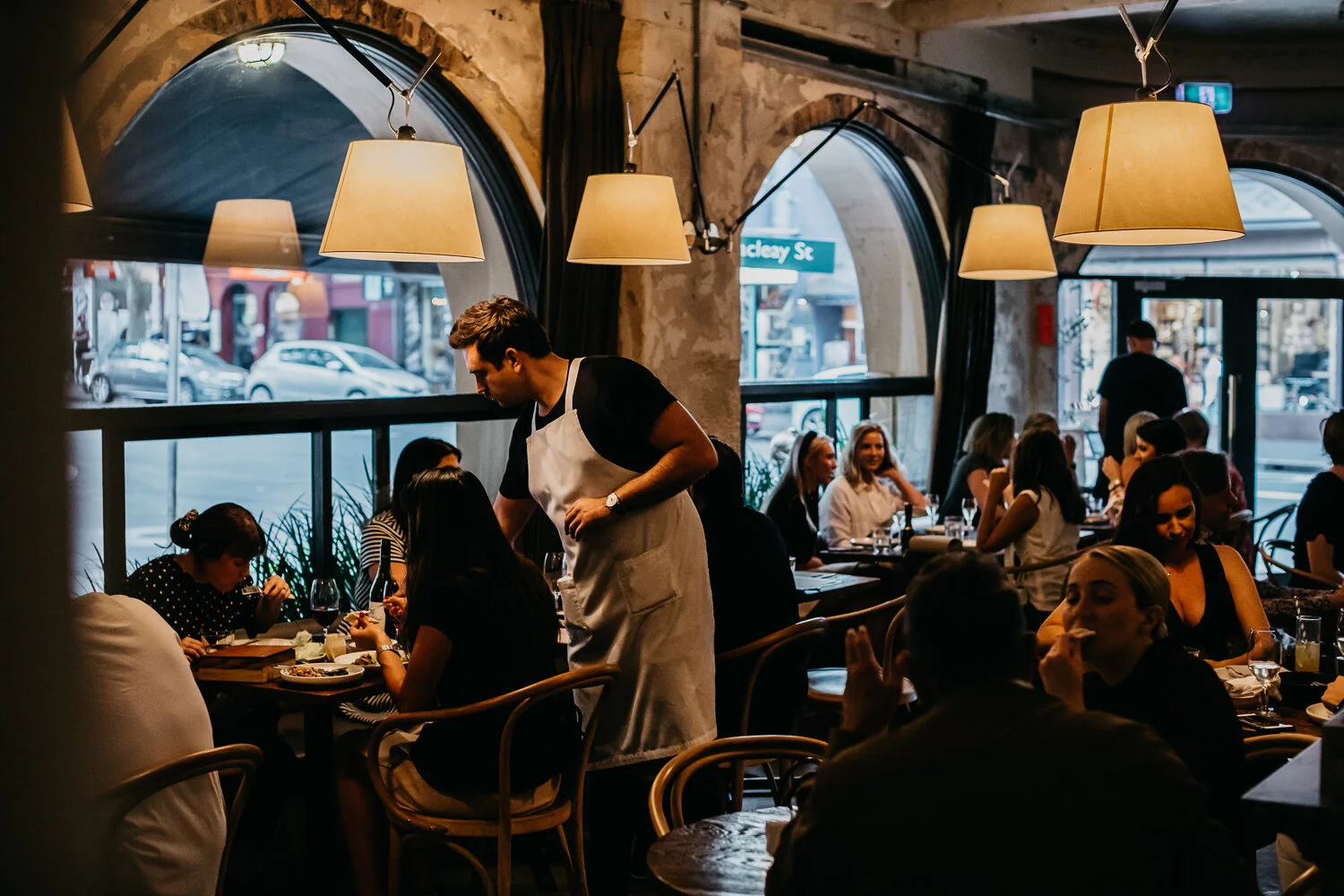 The Apollo dining room in Potts Point with warm lamps, arched windows and guests at tables.